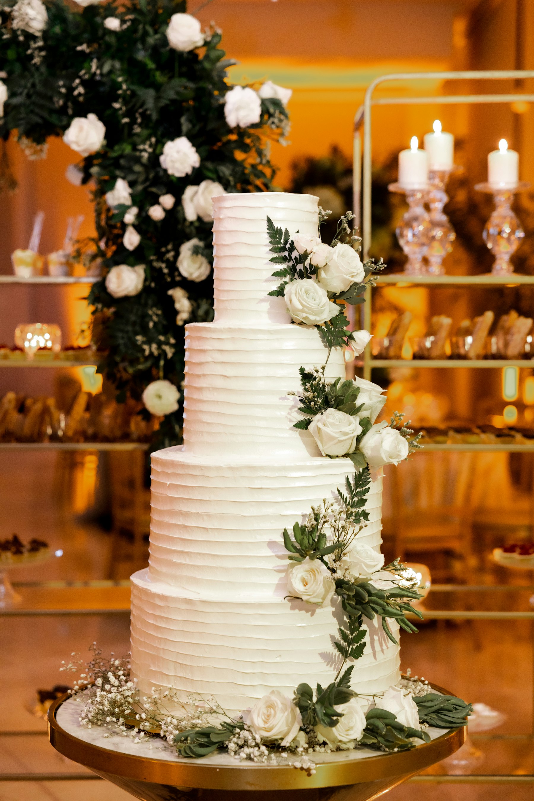 Tall white tiered wedding cake decorated with roses and greenery